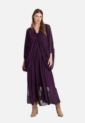 Un largo vestido morado y fluido hecho de tela ligera, con detalles de volantes en el escote y las mangas. Botas visibles por debajo.
