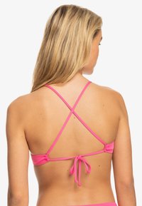 Roze bikini-top met verstelbare kruissnoeren aan de achterkant, voorzien van een strikdetail. Glad, rekbaar materiaal met een minimalistisch ontwerp.