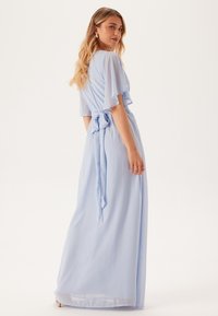 Robe maxi bleu clair avec des manches fluides et transparentes, et une taille nouée. Tissu doux et léger avec une texture lisse et une tombée subtile.
