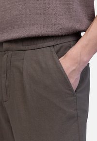 Donkere grijze broek met een elastische tailleband, zijzakken en een gladde textuur. Draag met een gestructureerde, lichtbruine top.