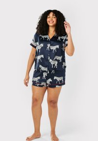 Marinblå pyjamasset med vita zebra-mönster; kortärmad skjorta med knäppning och matchande shorts med röda detaljer och en avslappnad passform.