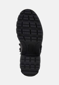 Semelle de chaussure en caoutchouc noir avec des crampons rectangulaires profonds et un logo central, vue de dessous sur un fond blanc.