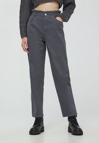 Pantaloni grigi a vita alta con un fit affusolato, dotati di tasche laterali e di una cintura elastica, abbinati a stivali neri con lacci.