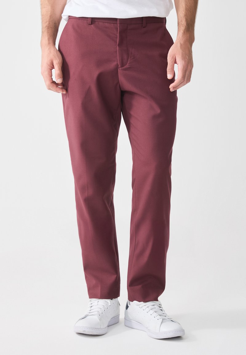 Burgundy pants made of woven fabric, featuring a slim fit design, straight legs, and side pockets. Paired with white sneakers.