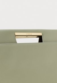 Mala de mão verde em pele com um fecho em metal dourado gravado com o nome da marca "Furla", design minimalista, textura suave.