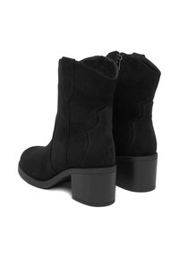 Černé semišové kotníkové boty s vrstveným podpatkem a zakřivenými švy. Zip na zadní straně usnadňuje obouvání. Měkká textura, elegantní design.