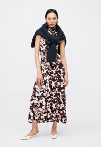 Μίντι φόρεμα με λουλουδένιο τύπωμα σε ροζ και μαύρο χρώμα με ψηλό λαιμό; συνδυασμένο με μπλε πλεκτό κασκόλ. Το μοντέλο φοράει λευκές γόβες με τακούνι.