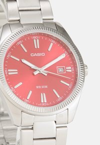 Montre en acier inoxydable argenté avec un boîtier rond, un cadran rouge, des index horaires blancs, un affichage de la date et un bracelet à maillons en métal. Résistante à l'eau jusqu'à 50 m.