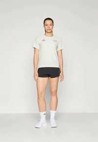 Heledad hallhallane spordisärk roosa aktsendiga, koos mustade lühikestega. Mudel seisab neutraalse tausta ees, jalas valged tossud ja sokid.