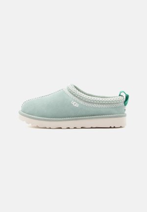 Green suede slip-on shoe with a white rubber sole, featuring decorative stitching around the collar and a small heel tab for easy wear.