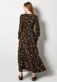 Abito maxi in un tessuto a fantasia che presenta toni terrosi di marrone, verde e bianco. Maniche lunghe, vita arricciata e gonna svasata.