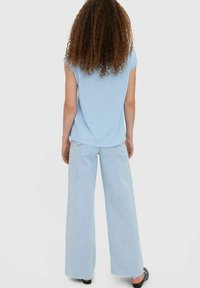 Jasnoniebieski top z krótkim rękawem w połączeniu z szerokimi spodniami z jasnego denimu. Tkanina wydaje się miękka, a krój jest luźny.