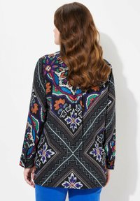 Blusa a maniche lunghe con motivo multicolore, caratterizzata da disegni floreali in viola, arancione e blu, su uno sfondo nero.