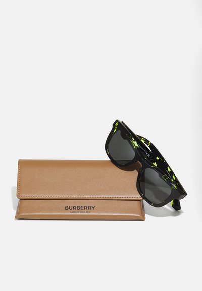 Ochelari de soare negri cu accente verzi pe un toc din piele bej. Tocul prezintă logo-ul 'BURBERRY' embosat. Ochelarii au o formă pătrată.