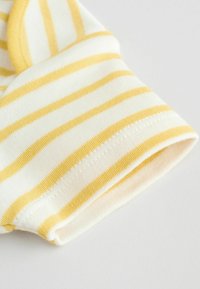 Žlté a biele pruhované textilné puzdro s jemným, textúrovaným povrchom. Má zavinutý lem a starostlivé stehovanie pozdĺž okraja.