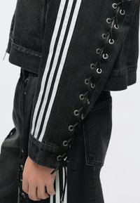 Μαύρο τζιν μπουφάν με λευκές ρίγες, διακοσμημένο με κορδόνια κατά μήκος του μανικιού με μεταλλικά χυτό, υφή υφάσματος και cropped σχέδιο.