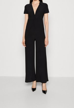 Mono negro con un escote en V profundo, mangas cortas y pantalones de pierna ancha. Fabricado con un tejido suave y con pliegues en la parte delantera.
