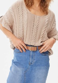 Suéter de punto beige con un corte suelto y patrón de trenzado, combinado con una falda de mezclilla azul clara y un cinturón marrón con una hebilla dorada.