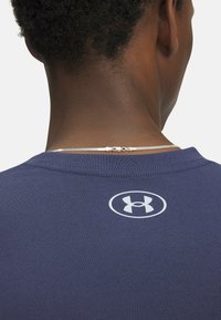 Camisa de manga corta azul marino con escote redondo y un logo blanco de Under Armour impreso en la parte trasera, hecha de tela suave y ligera.