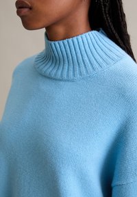 Lichtblauwe gebreide trui met een hoge ribbelhalslijn, voorzien van een zachte, textuurstof en een relaxed fit ontwerp.