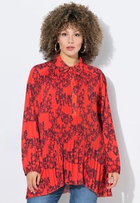 Blusa rossa con bottoni, decorata con un motivo testuale nero, maniche lunghe, design plissettato e vestibilità rilassata. Abbinata a jeans blu.