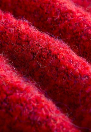 Rotes Strickgewebe mit einer strukturierten Oberfläche und erhabenen Fasern, die ein weiches und flauschiges Aussehen erzeugen. Bemerkenswerte Variationen in den Rottönen.
