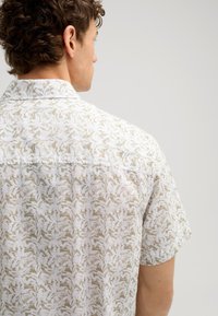 Kurzarmhemd mit einem weißen Blumenmuster auf einem hellbeigen Hintergrund, aus leichtem Stoff mit entspannter Passform.