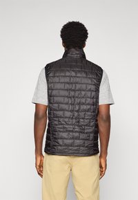 Black sleeveless puffer vest with a high collar, featuring a quilted pattern and smooth texture, worn over a gray t-shirt.