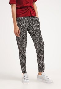 Housut mustavalkoisella kuviolla, slim fit -malliset ja elastisella vyötäröllä, yhdistettynä harmaisiin lenkkareihin ja punaiseen lyhythihaiseen puseroon.