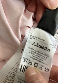 Light pink fabric with a smooth texture, showing a care label featuring icons for washing and care instructions, and branding details.