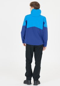 Blå och marinblå vattentät jacka, med huva, slät textur och kontrasterande färgblockdesign, bärs med svarta byxor och stövlar.