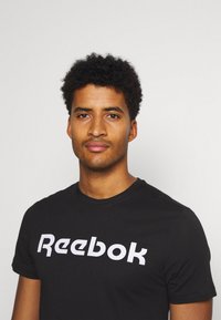 Svart bomull t-skjorte med en fremtredende hvit Reebok-logo på forsiden, kortermet og med rund hals.
