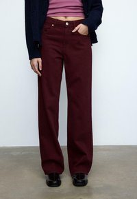 Burgunderfarvede jeans med vidt ben, frontlommer, knap- og lynlåslukning, lavet af denimstof. Stylet med en tætsiddende top og mørke sko.