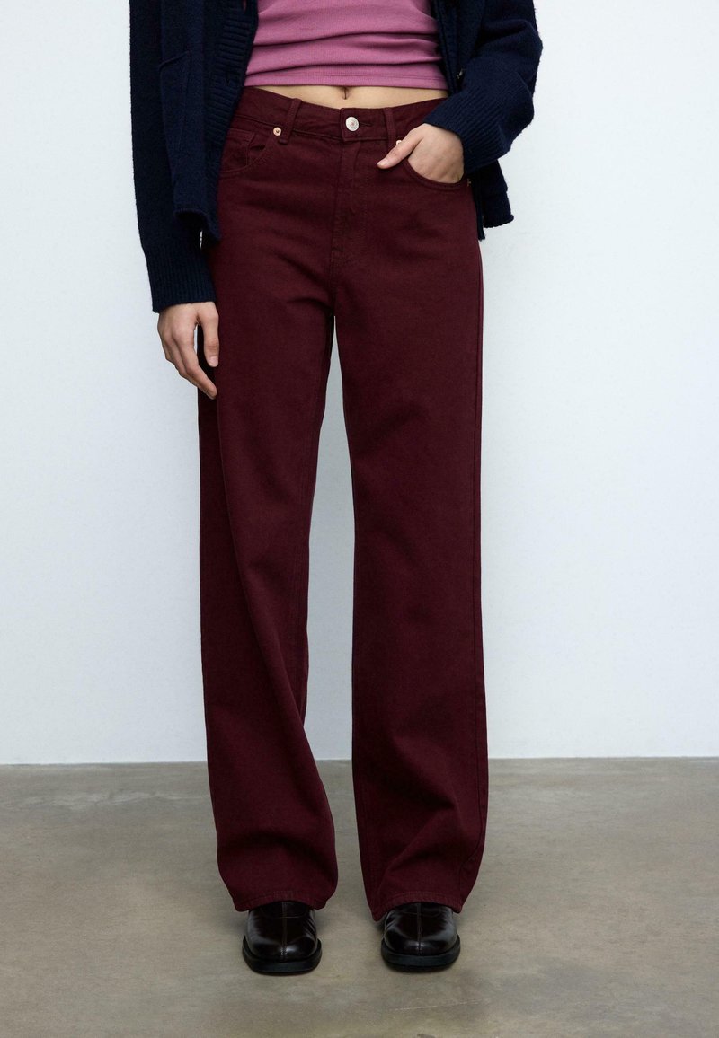 Burgunderfarvede jeans med vidt ben, frontlommer, knap- og lynlåslukning, lavet af denimstof. Stylet med en tætsiddende top og mørke sko.