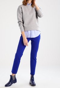 Grauer Hoodie, hellblaues Hemd mit Kragen, leuchtend blaue Slim-Fit-Hosen und glänzende dunkelblaue Ankle Boots mit elastischen Seiteneinsätzen für zusätzlichen Komfort.