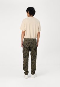 Beige katoenen T-shirt en olijfgroene camouflage cargo broek met zijzakken, aansluitend ontwerp en elastische manchetten, gecombineerd met witte sneakers.