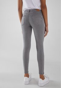 Vaqueros skinny grises con una textura suave, que presentan una cintura alta, dos bolsillos traseros y un parche de cuero de la marca en la parte trasera.
