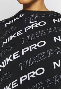 Maglietta sportiva nera con un motivo di testo bianco ripetuto "NIKE PRO". Tessuto morbido con scollatura rotonda e maniche corte.
