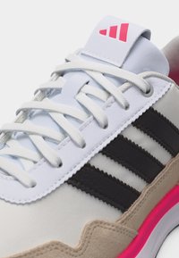 Valge toss mustade triipude, beežide seemisnahast detailide, valgete nööride ja roosa tallakujundusega, keel nähtaval punase logoga.