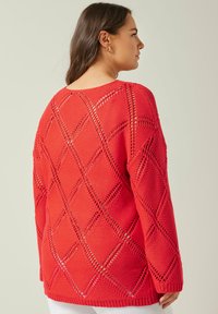 Röd stickad tröja med diamantmönstrade utskärningar, långa ärmar och en avslappnad passform. Ribbstickade ärmslut och nederkant för extra textur.