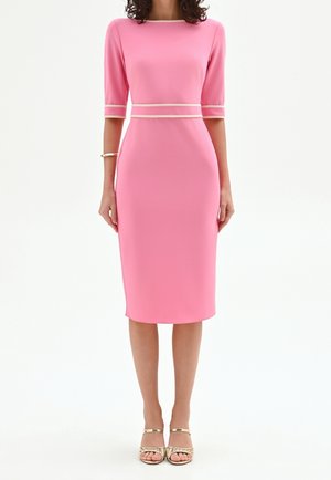 Femme portant une robe midi rose ajustée avec des manches trois-quarts et une bordure claire à la taille et aux poignets, associée à des talons ouverts dorés.