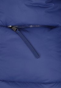 Prim-plan cu un fermoar albastru închis, parțial deschis, cu un mâner din material textil, pe o suprafață căptușită din material textil.