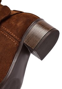 Stivale alla caviglia in suede marrone con tacco texturizzato, punta rotonda e cuciture a contrasto lungo la cucitura superiore. Suola in gomma per una buona aderenza.