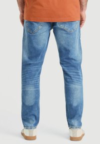 Vaqueros de mezclilla azul claro con un lavado ligeramente desteñido, corte de pierna recta y dos bolsillos traseros. Combinados con zapatos beige que tienen una suela texturizada.