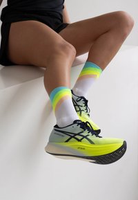 Neon yellow running shoes with black laces and logo, paired with white socks featuring multicolored stripes in green, blue, and peach.