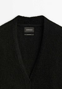 Pull en maille noir avec col en V, avec une étiquette portant la mention "Massimo Dutti Limited Edition" et "Made in China."