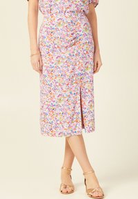 Rosa Midikleid mit bunten Blumenmustern, einem seitlichen Schlitz und leichtem Stoff, kombiniert mit metallischen Riemchensandalen.