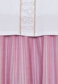 Haut blanc avec des détails en strass épelant "1961", associé à une jupe en tulle rose et scintillante avec des rayures verticales.