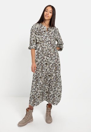 Langes Blumenkleid mit einem Knopfdesign, umgeschlagenen Ärmeln und einem gerafften Rock. Kombiniert mit beigen Schnürstiefeln.