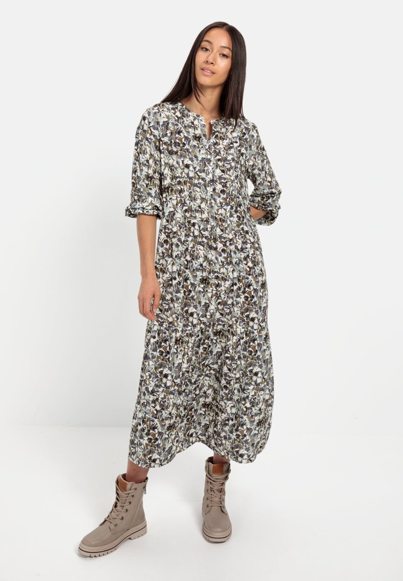 Langes Blumenkleid mit einem Knopfdesign, umgeschlagenen Ärmeln und einem gerafften Rock. Kombiniert mit beigen Schnürstiefeln.